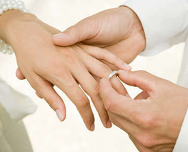 The groom slides the wedding band on the bride's finger