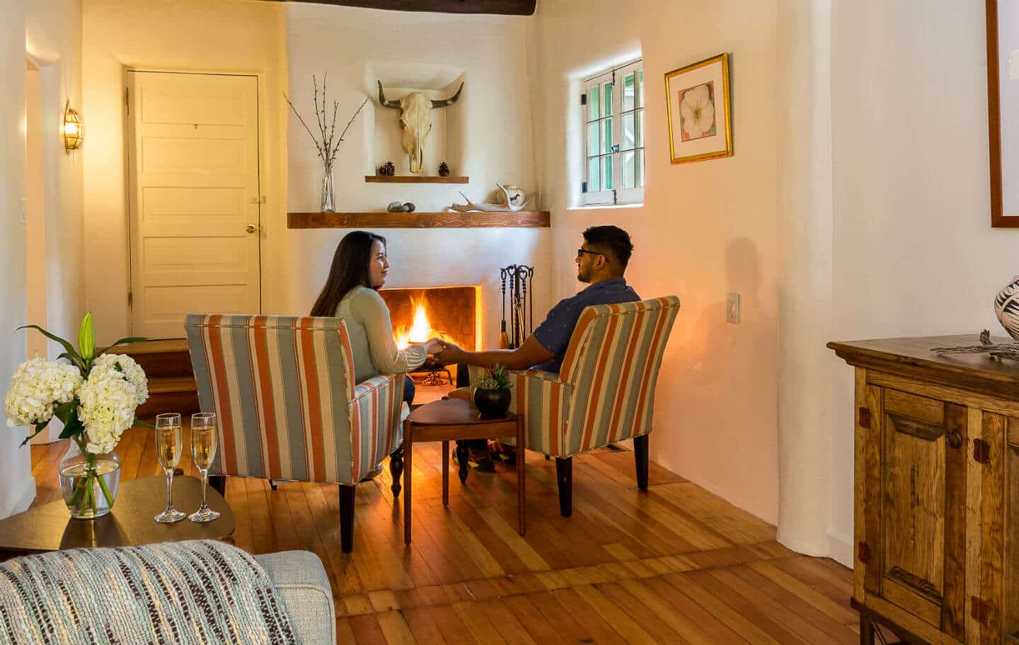 Couple sitting holding hands in front of burning fire in fireplace in the Georgia Okeeffe guest room