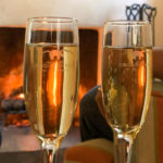 Champagne flutes sparkling in front of burning fire in fireplace