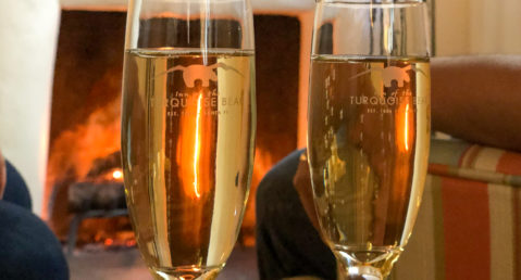 Champagne flutes sparkling in front of burning fire in fireplace