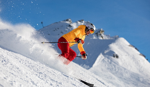 Downhill skier in bright clothng with snow flying behind