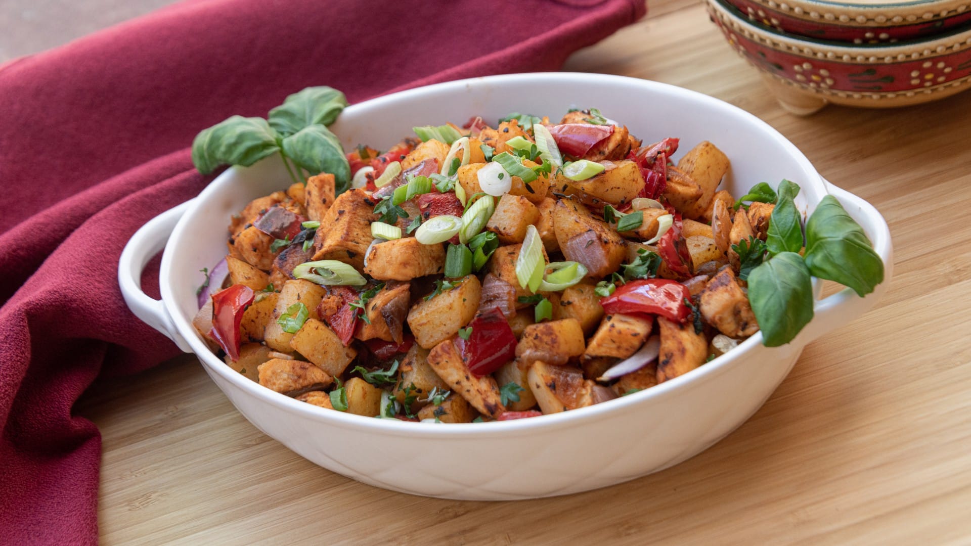 White serving bowl of Sweet Basil Chicken Hash including diced chicken, potatoes, red peppers, red onions, green onions, parsley and sweet basil