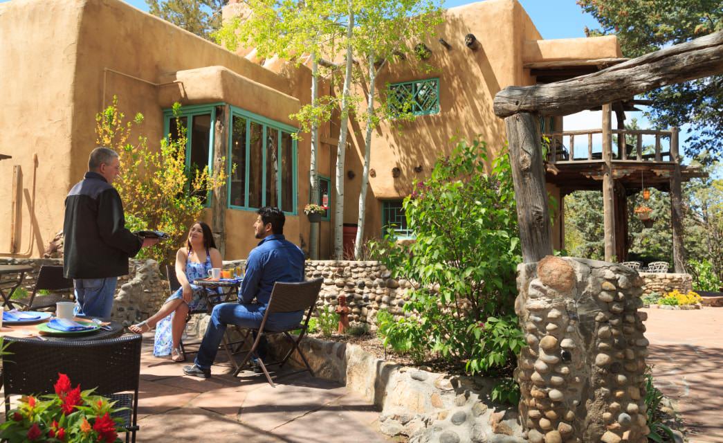 Couple sitting on patio of large adobe home speak to the innkeeper at breakfast.
