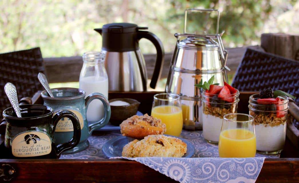 Breakfast tray with coffee, scones, juice, and yogurt parfaits on patio table outdoors.