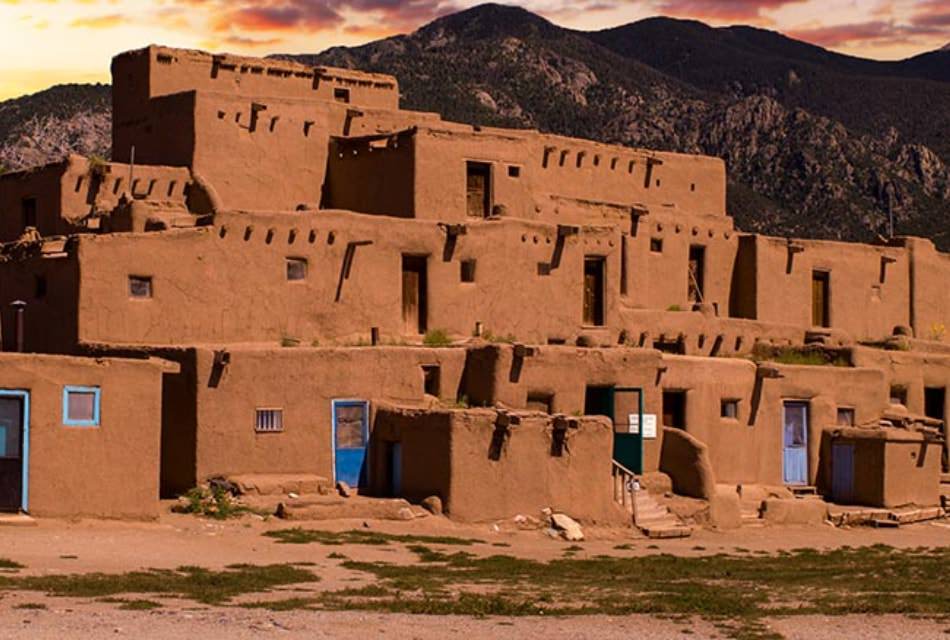 Adobe building with blur-painted doors and blue window frames in front of mountains.