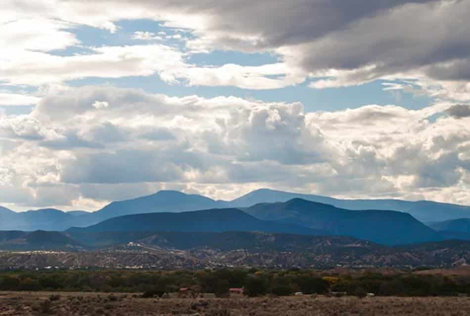 Long-range view of blue mountain range under wide Western sky with clouds.