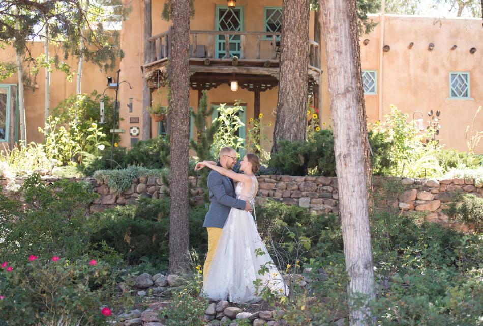 Happy wedding couple embracing in garden of beautiful adobe building.