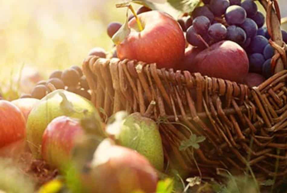 Wicker basket of fruit including apples, pears, plums and purple grapes.