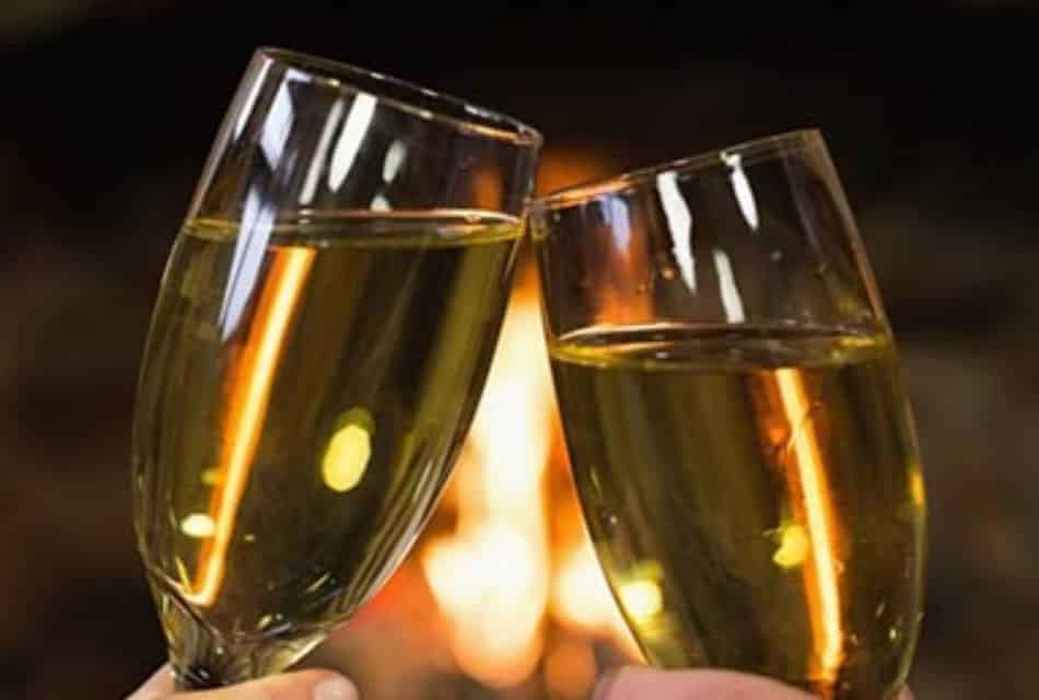 Champagne flutes clink together in front of fire.