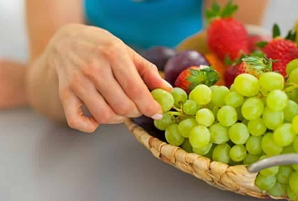 Woman plucking a green grape from a basket of fruit.