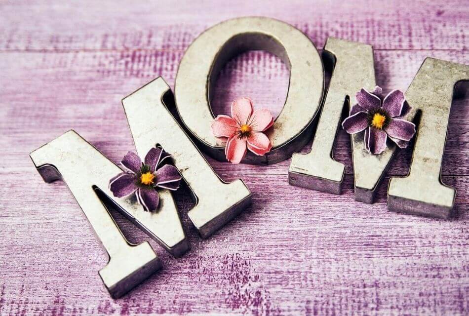 MOM spelled out in gold letters with floral enhancements on a wooden background