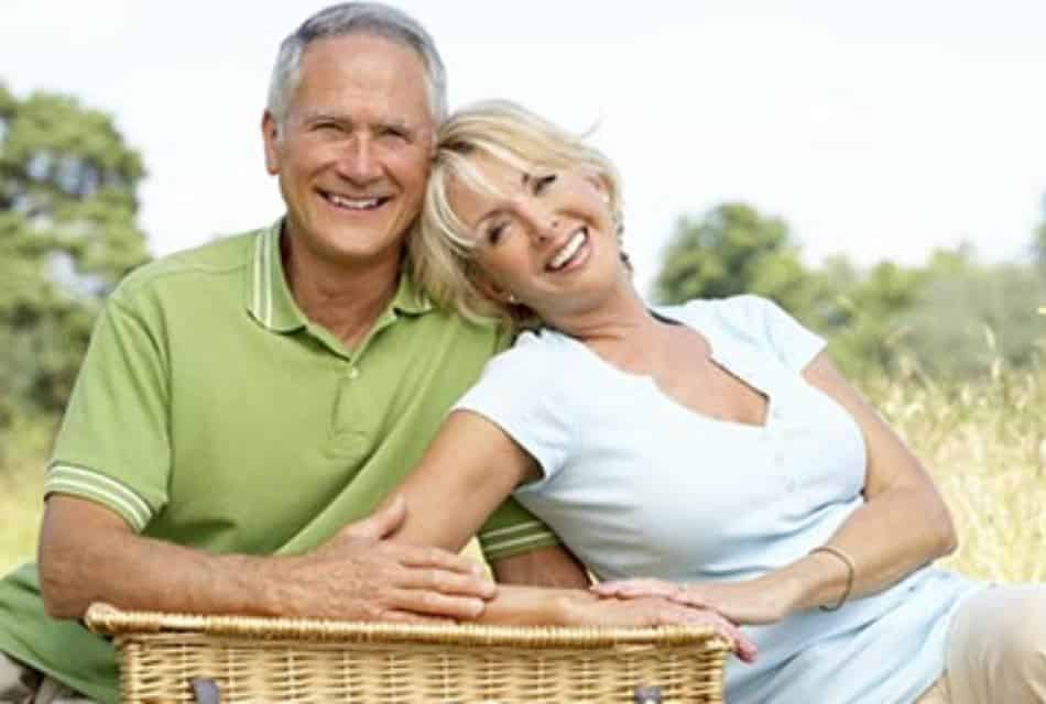 Attractive older couple happily lean on wicker picnic box outdoors.