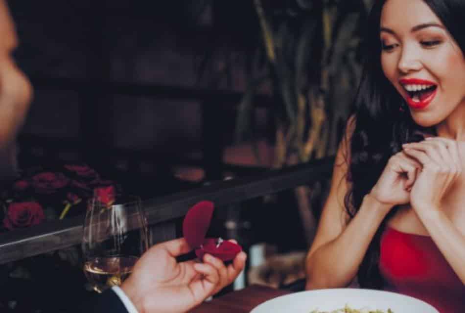 Beautiful dark-haired woman in red gasps at engagement ring in a velvet box.