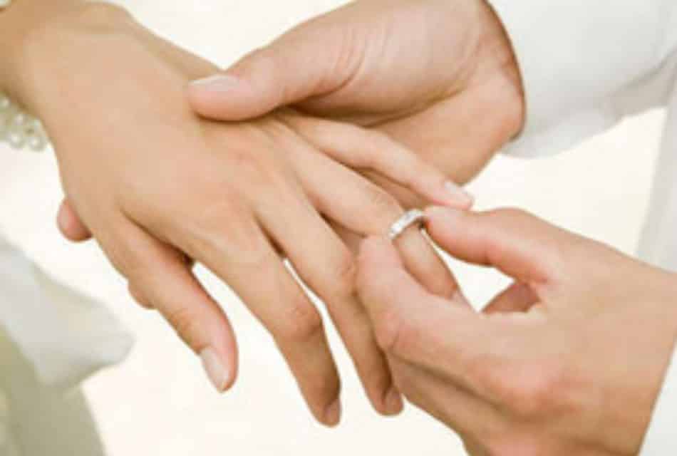 Male hands putting a silver wedding band on a woman's hand in wedding ceremony.