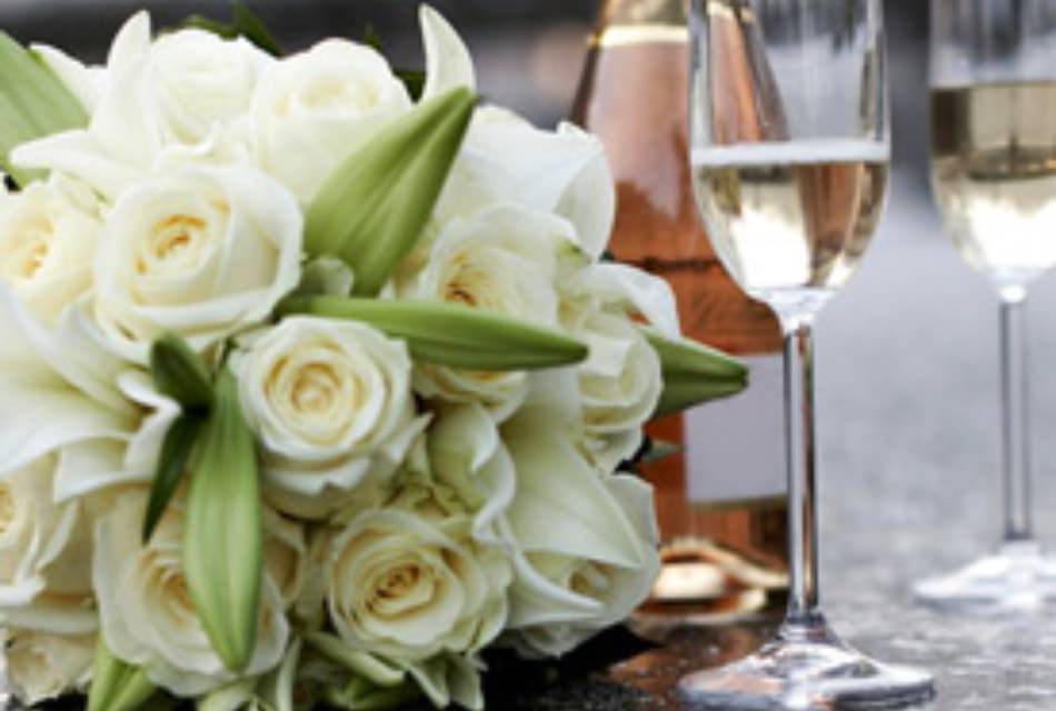 Bouquet of white roses next to two champagne flutes on a table with a wine bottle.