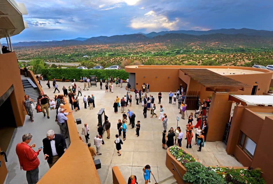 Party crowd on steps and patio of a large adobe rooftop structure.