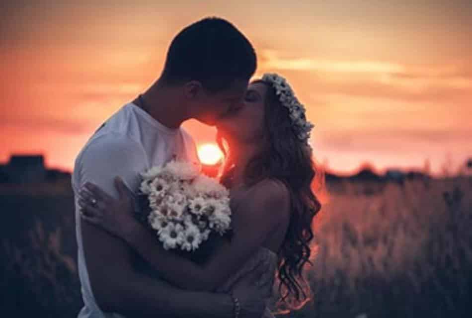 Young wedding couple kiss in front of beautiful orange sunset.