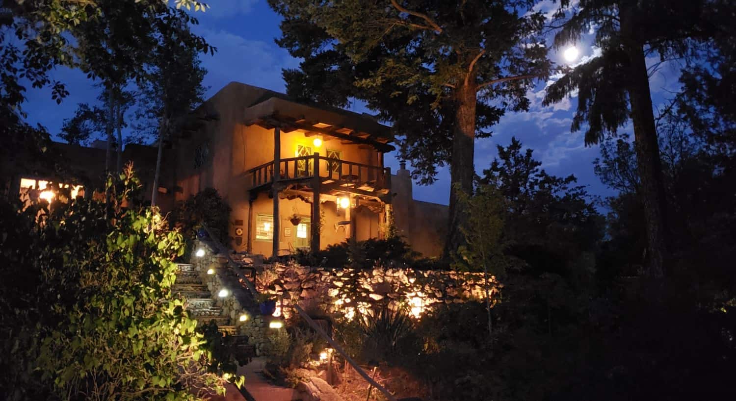 Exterior view of the property at dusk surrounded by large green trees, green vegetation, stone walkways, and lighting
