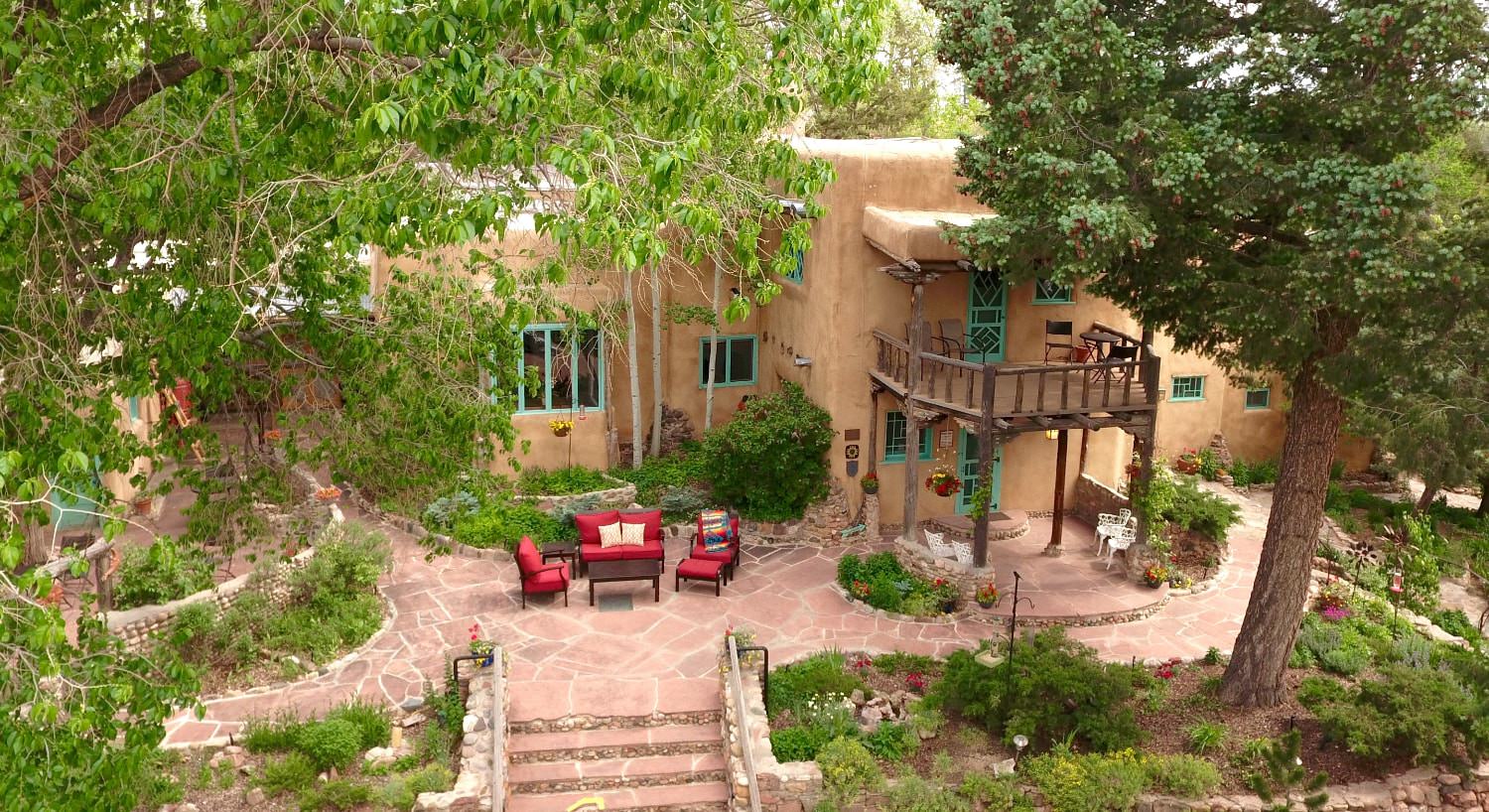 Exterior view of the property surrounded by large green trees, green vegetation, stone walkways, large patio, and red cushioned patio furniture