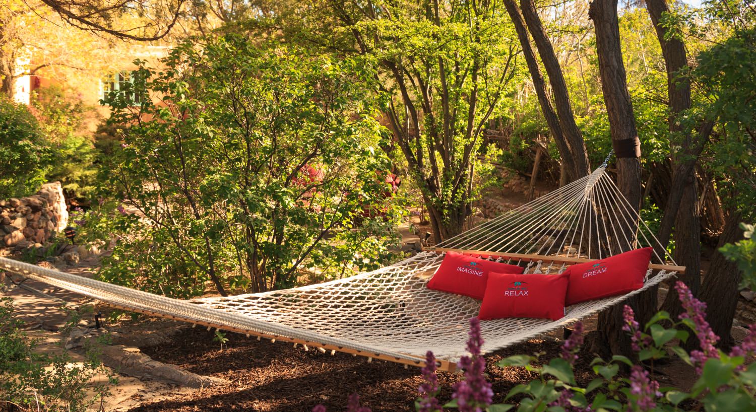 Hammock with red pillows surrounded by green bushes and trees