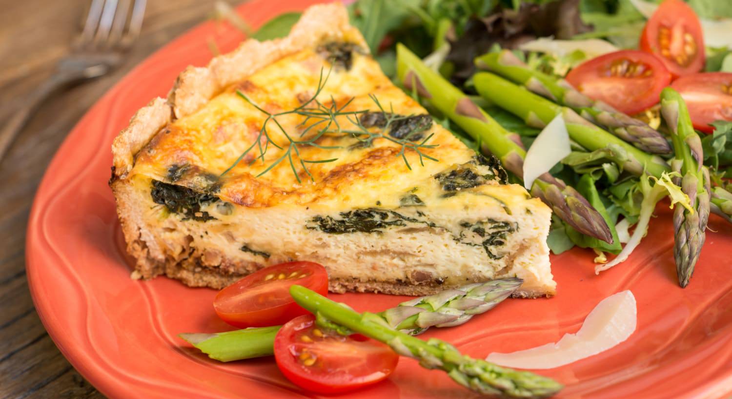 Orange plate with quiche, sliced tomatoes, lettuce, and asparagus