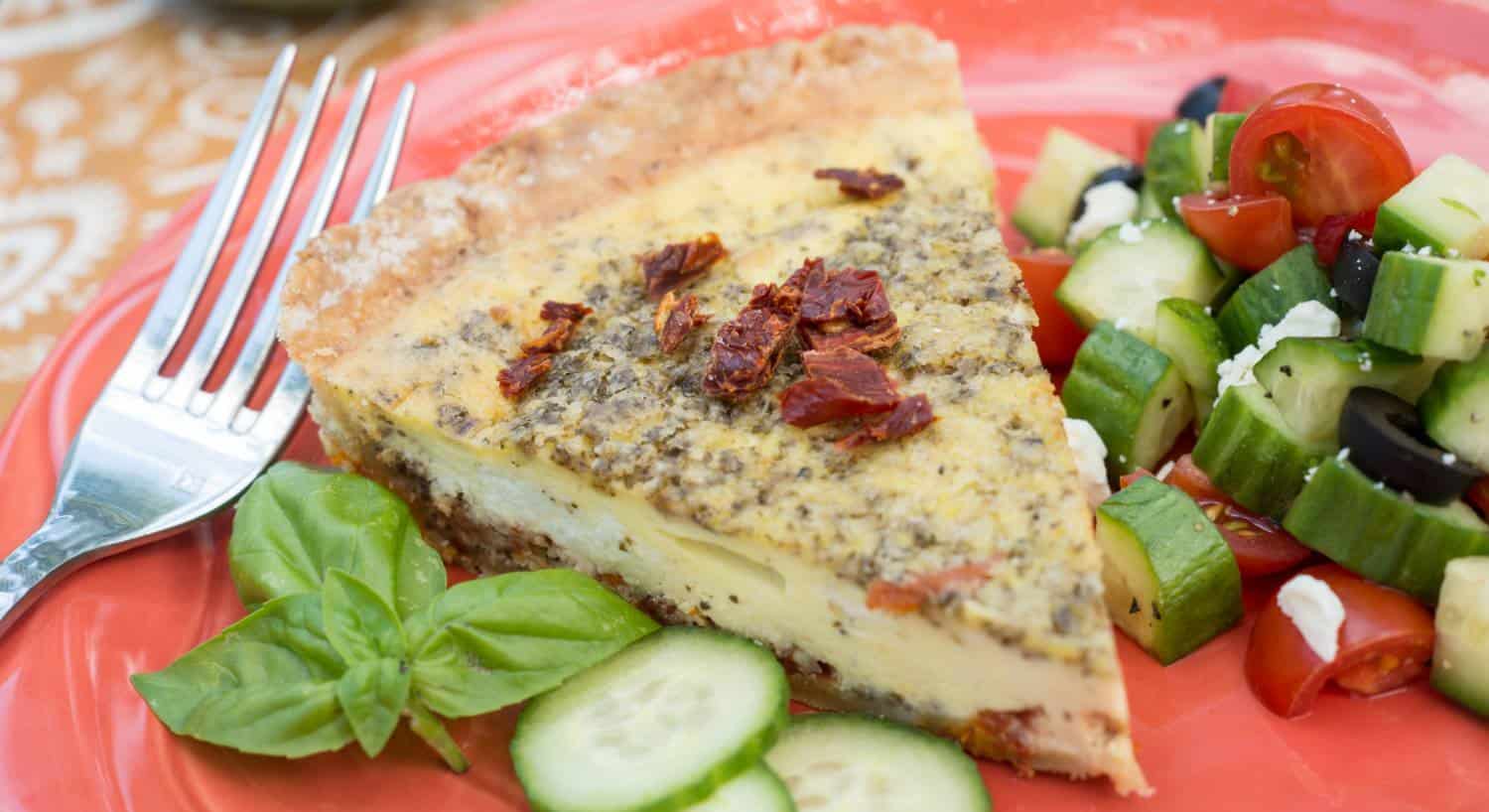 Orange plate with quiche and sliced cucumbers, tomatoes and olives