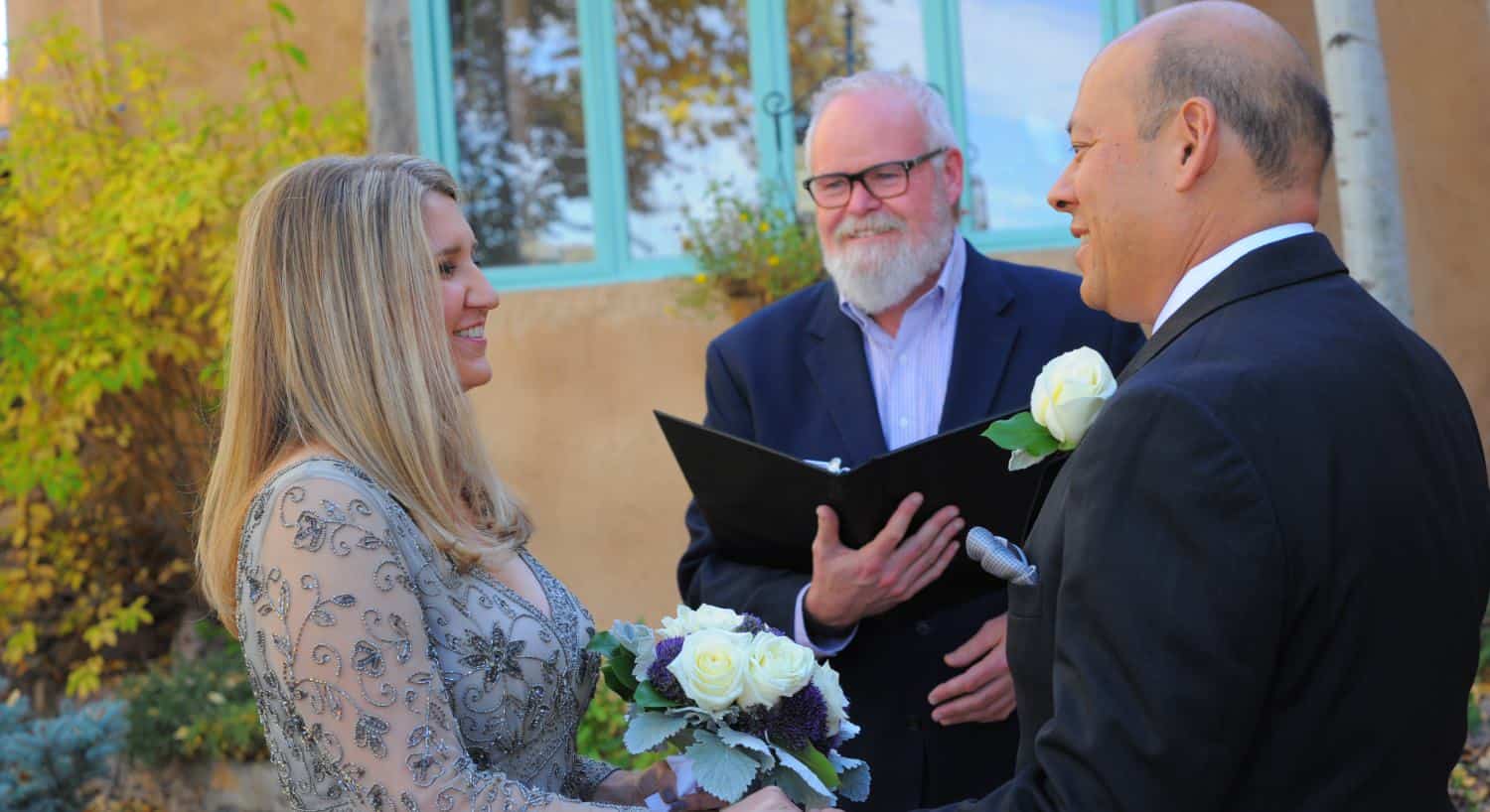 Bride and groom standing and looking at each other with officiant smiling at them