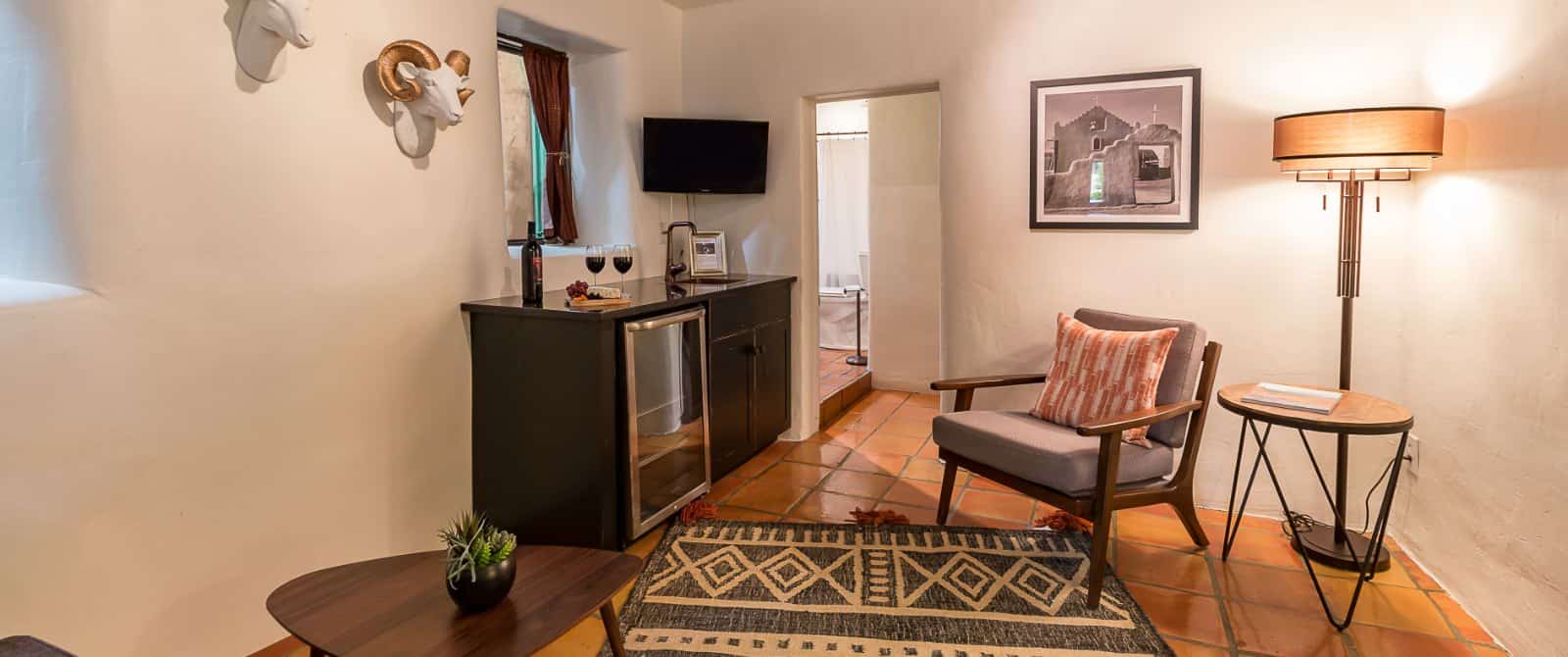 Sitting area in suite with wine fridge, tv, and two tables with chairs.