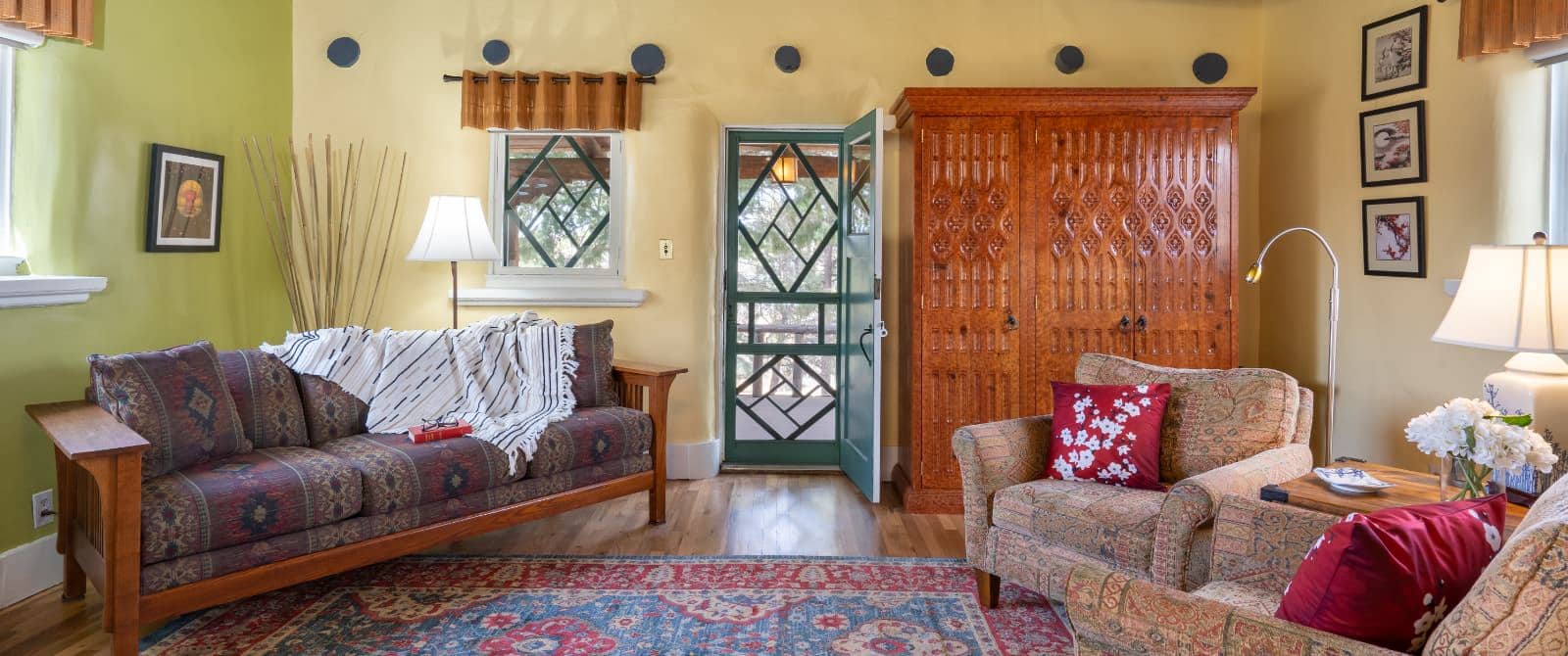 Bedroom sitting area with Asian-style rug, two armchairs and a wooden sofa upholstered with Southwestern fabric next to large wooden armoire.