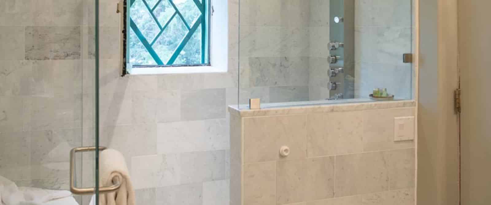 Modern white marble-tiled shower with multi-head sprayer and glass doors.