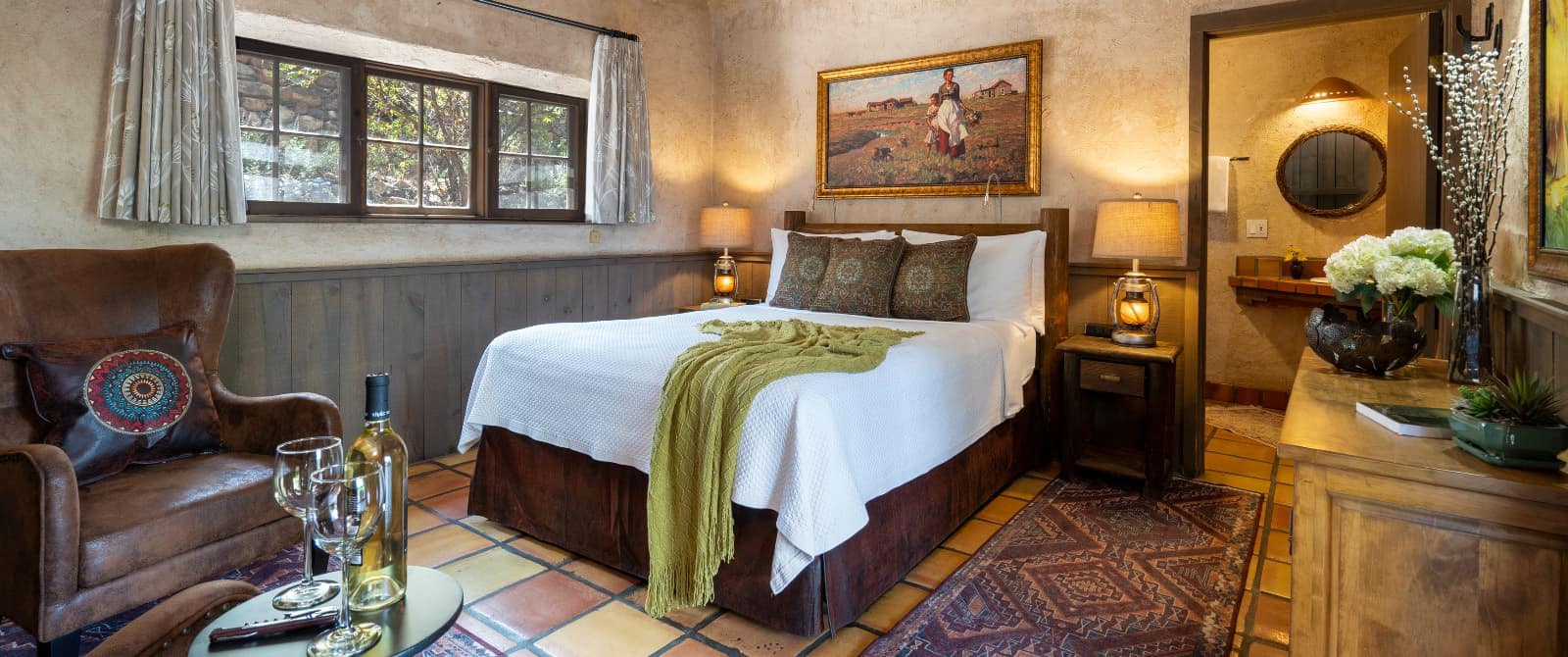 Bedroom with planking chair-rail, terra-cotta tile floor, leather armchair and queen bed with white coverlet.