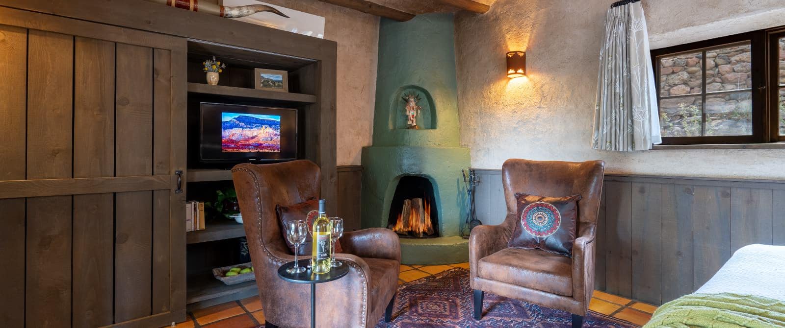 Green fireplace in Southwestern-style next to large wooden armoire, fronted by leather armchairs.