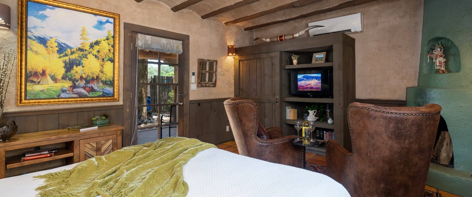 Southwestern-style bedroom with fireplace, leather armchairs, wooden armoire and queen bed in white.