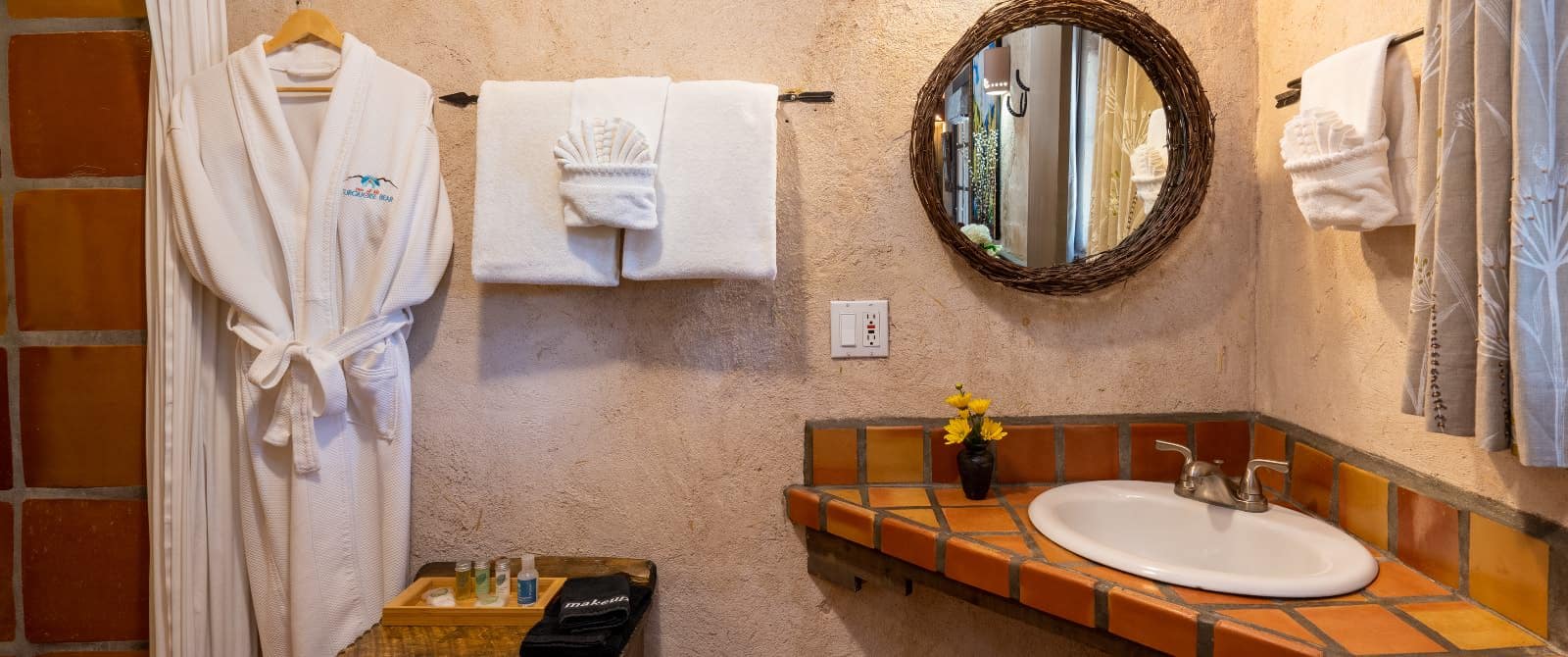 Corner brick-counter sink in bathroom with stucco walls, cushy robe and white towels.