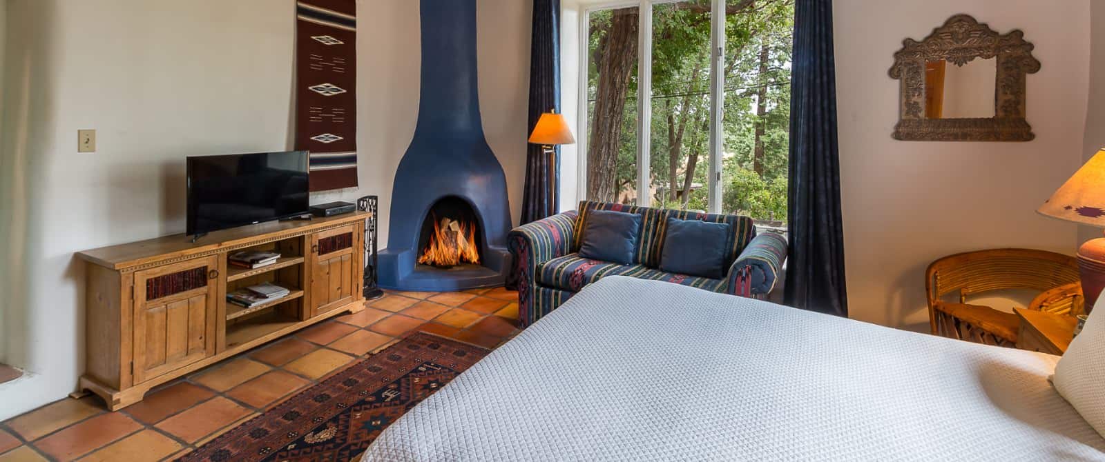 Attractive blue fireplace in bedroom with Saltillo tile floor, bed made up in white and southwestern-style sofa.