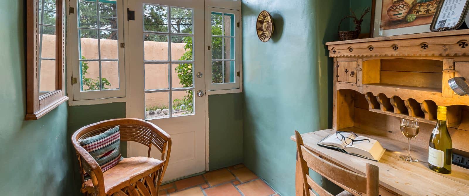 Cool turquoise walls frame a wooden door next to a chair and desk with a book and wine bottle.