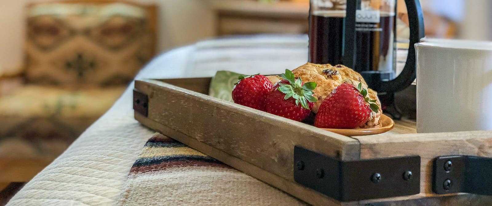 Strawberries and scones with French-press coffee on a wooden tray in bedroom.