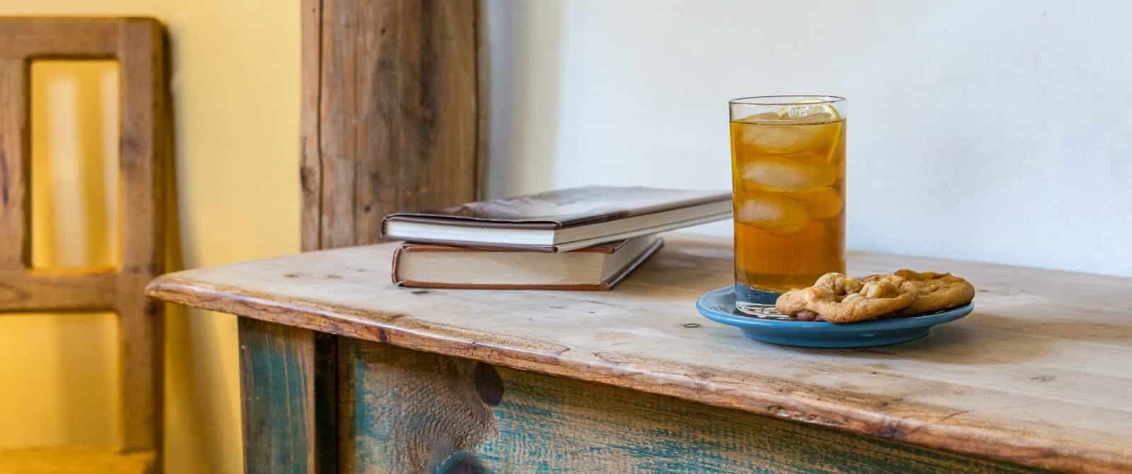 Cookies and iced tea on a blue plate next to stacked books on a distressed wooden dresser.