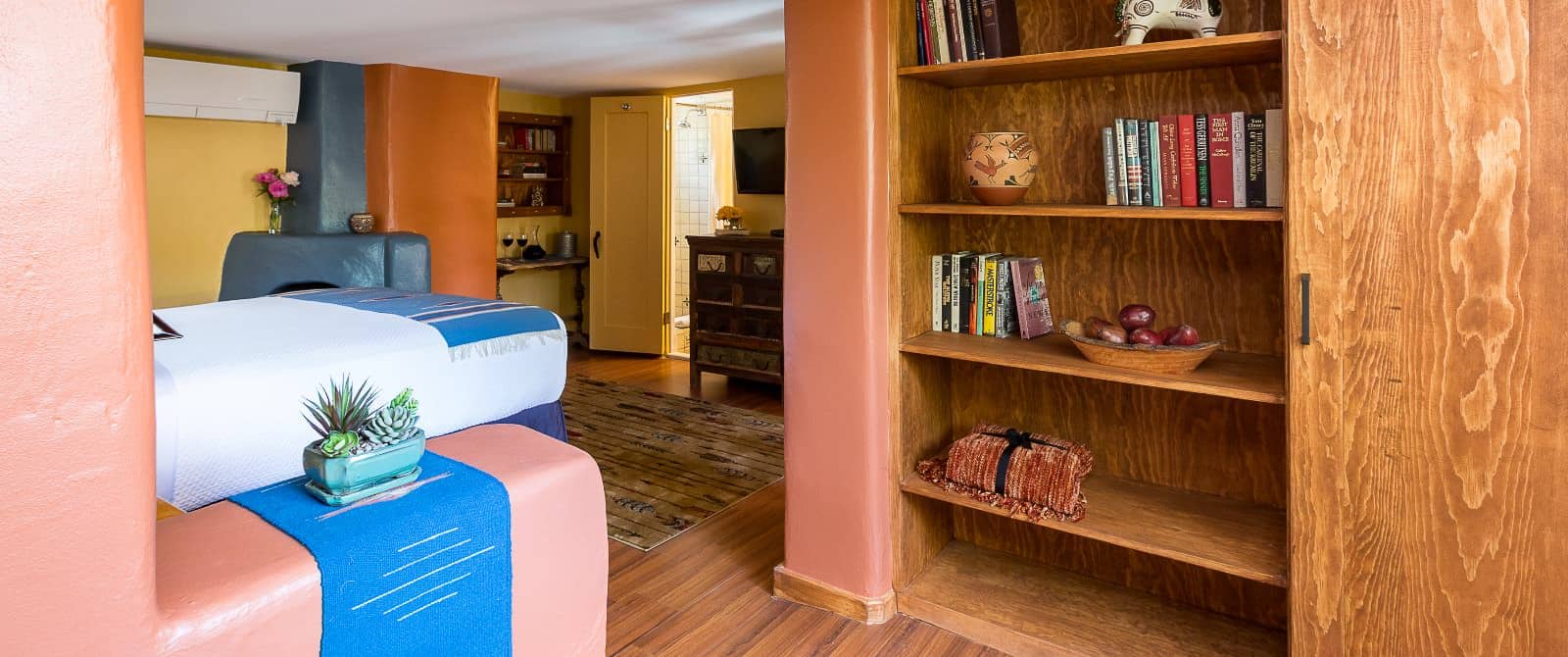 Bedroom with wood floors, tidy bed made up in white and blue and a built-in wood bookcase.