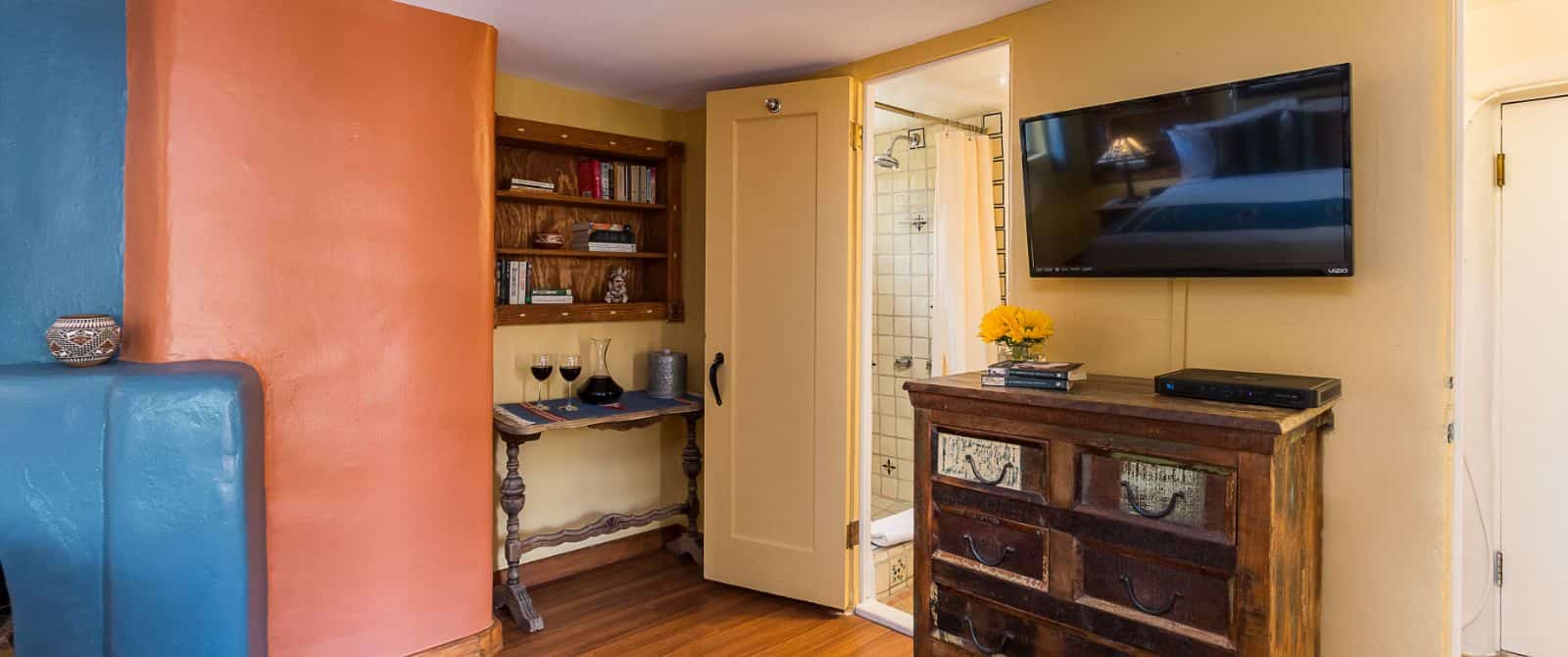 Bedroom with cream, adobe, and blue-painted walls, wood floors, and tiled bathroom.