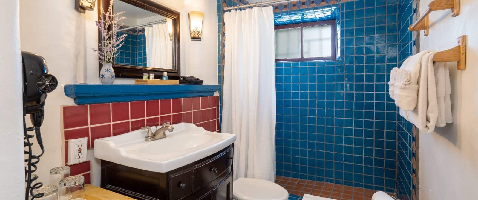 Bathroom with blue-tiled shower and red tile backsplash over the sink vanity with white shower curtain and towels.