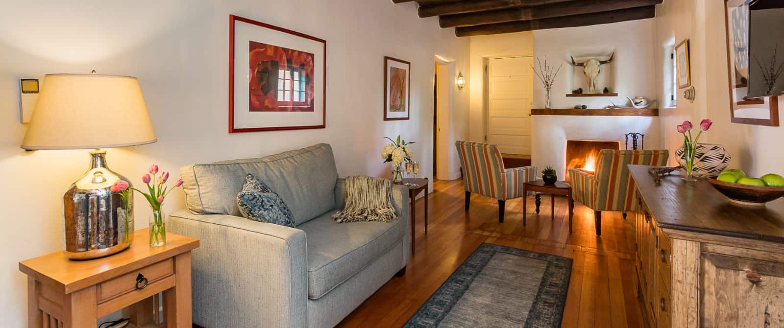 Sitting area of guest room with sofa, tv, two striped armchairs and wood-mantled fireplace.