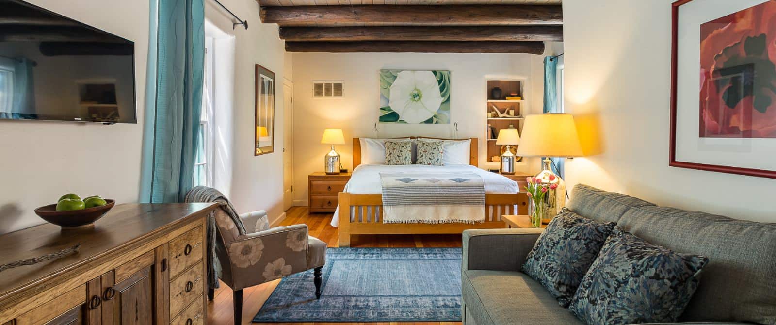 Tastefully decorated bedroom with wooden ceiling beams, plank flooring and a king bed with Georgia O'Keefe prints on the walls.