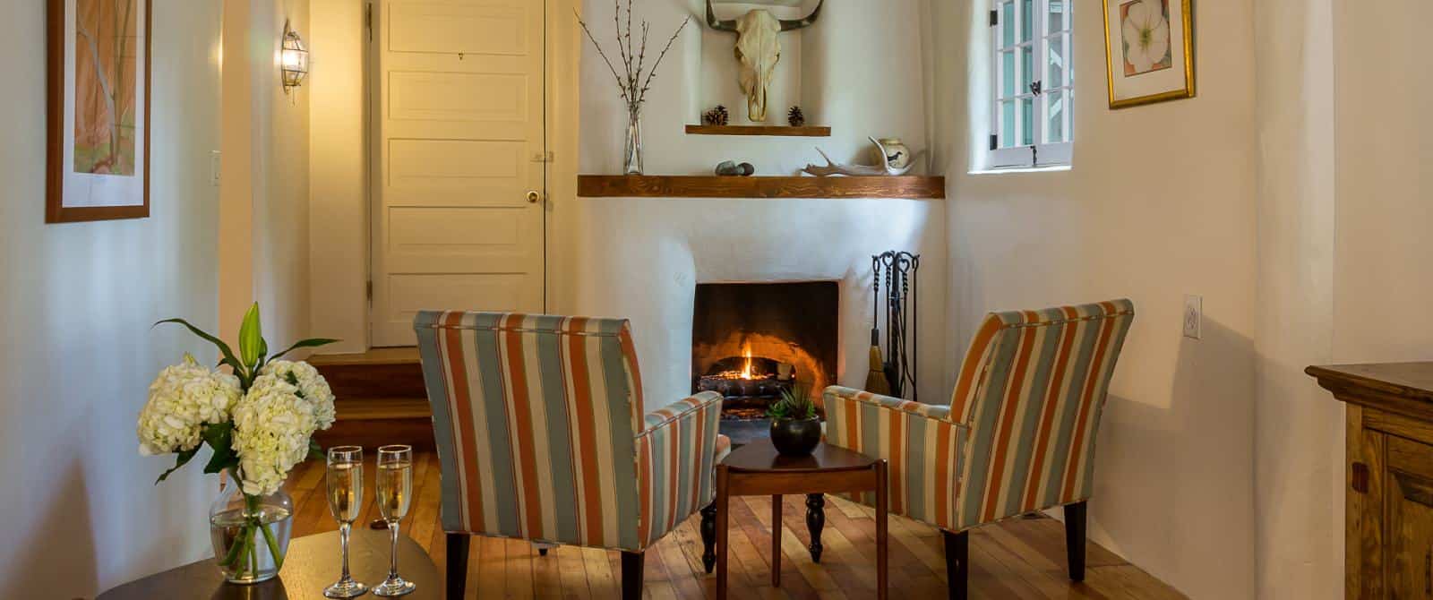 Beautiful southwestern plastered fireplace fronted with two striped armchairs, a mid-century end table and wood plank flooring.