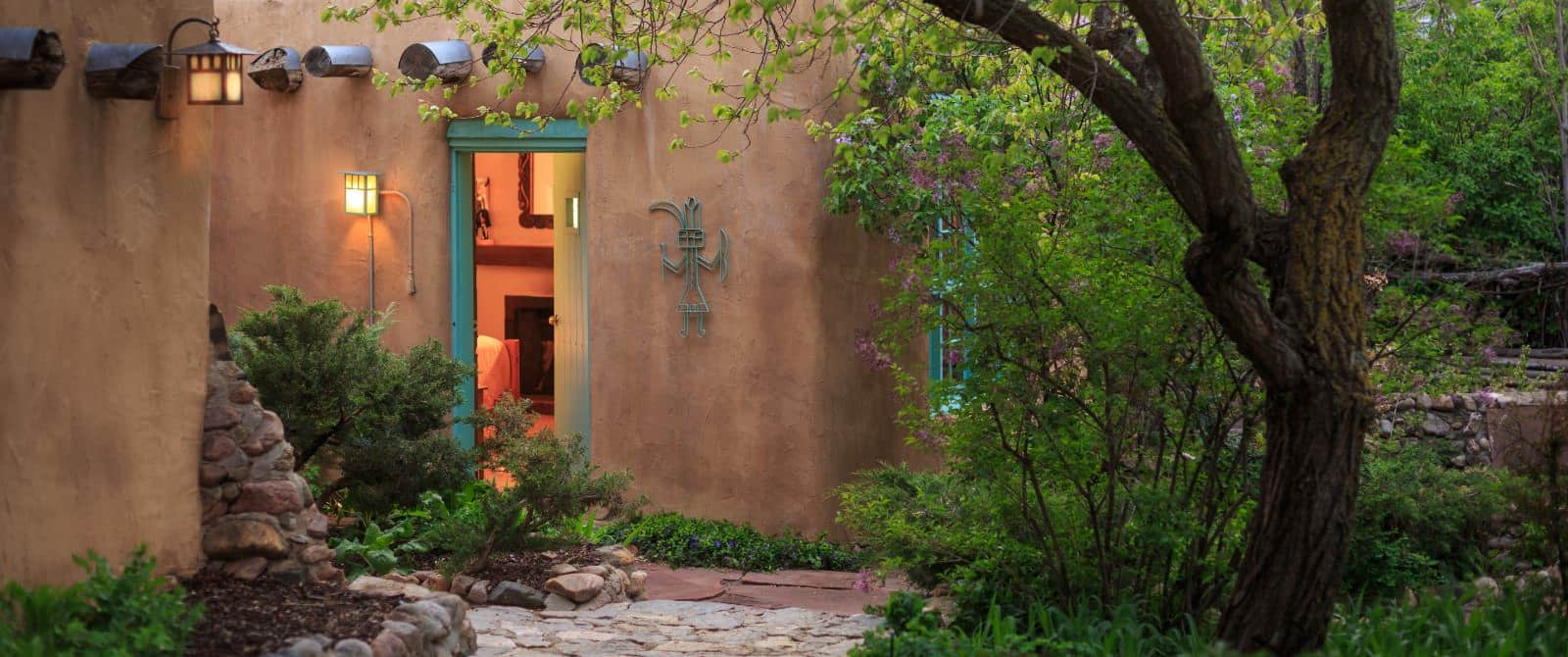 Exterior door to stone walkway from bedroom in tan adobe building with a warrior iron art piece on wall.