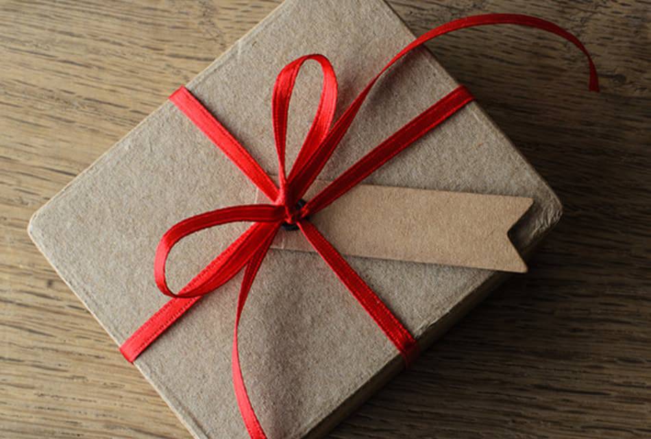 Textured brown paper box tired with a red ribbon on a wooden surface.