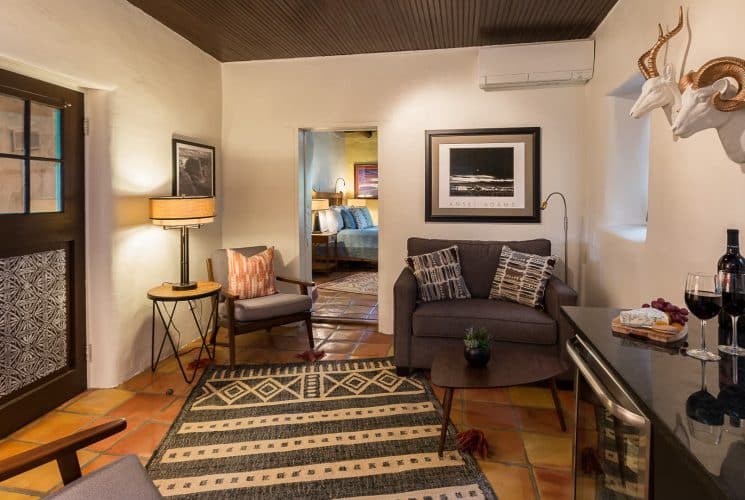 Sitting area in suite with wine fridge, tv, and two tables with chairs, decorated in modern Southwest style.