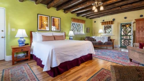 Guestroom with wooden floors, blue and red rugs, wooden furniture and bed made up in white and maroon.