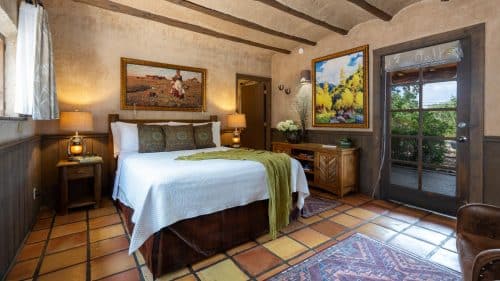 Bedroom with planking chair-rail, terra-cotta tile floor, wooden beams in ceiling and queen bed with white coverlet.