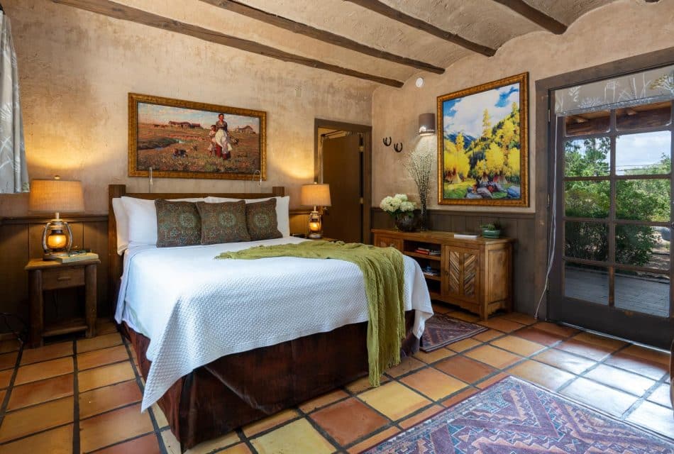 Bedroom with planking chair-rail, terra-cotta tile floor, wooden beams in ceiling and queen bed with white coverlet.